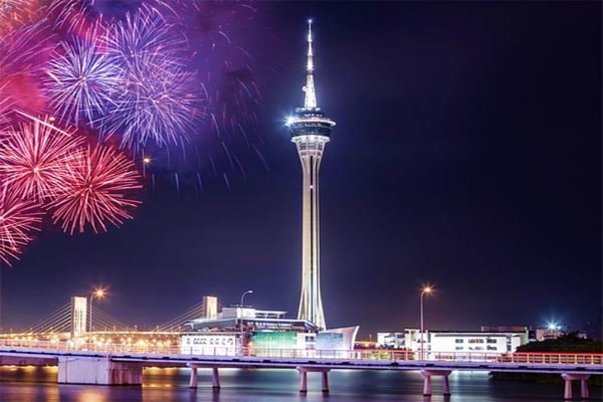 Stratosphere Tower in Las Vegas at night with pink and purple fireworks exploding over the illuminated skyline and water refl