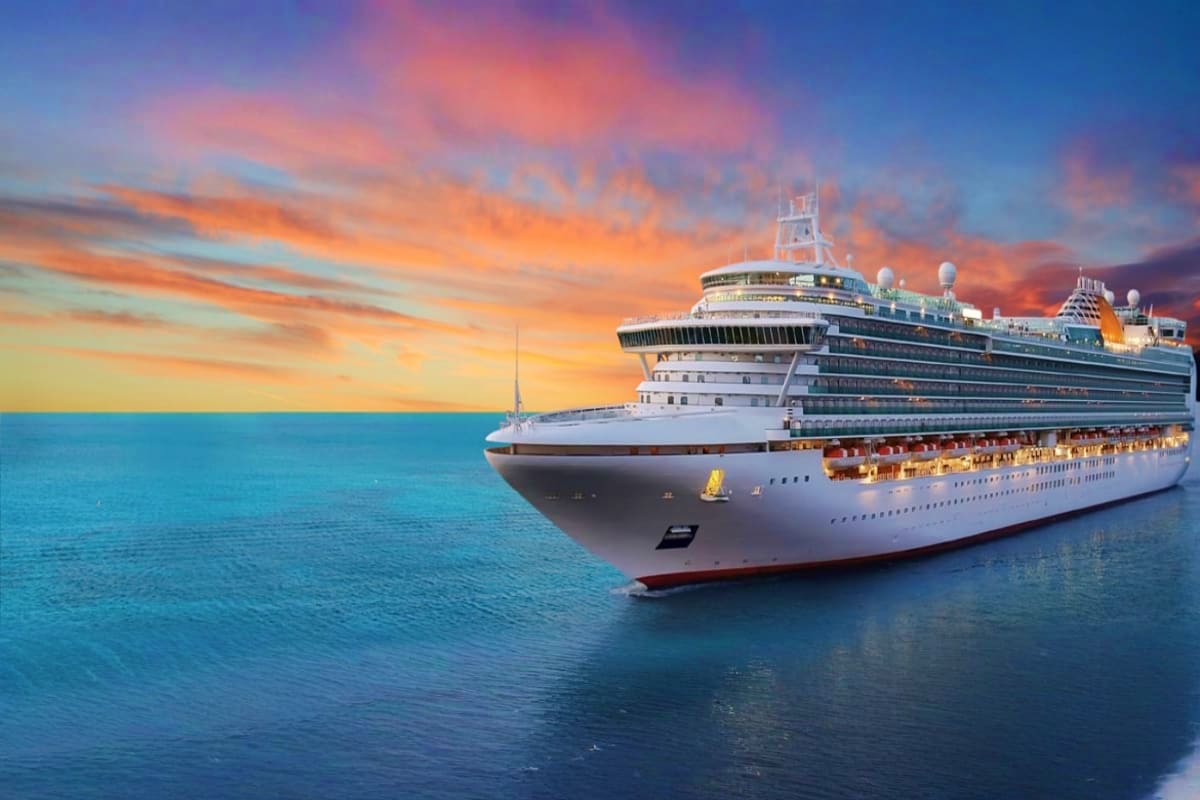 Large modern cruise ship on turquoise ocean waters at sunset with orange and pink sky