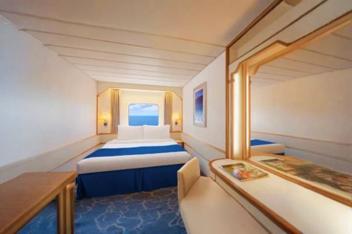 Luxury cruise ship cabin with queen bed, ocean view window, wooden trim, gold lighting, and modern furnishings