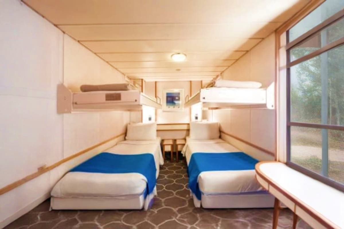 Interior of Cordelia cruise ship cabin with two beds with blue blankets, upper berths, window, and modern amenities