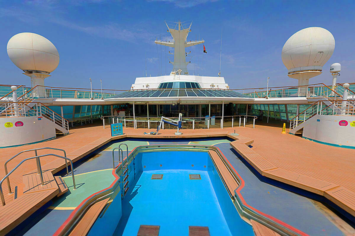 Cordelia cruise ship deck with swimming pool, teak wood flooring, satellite domes, and tall funnel under blue sky