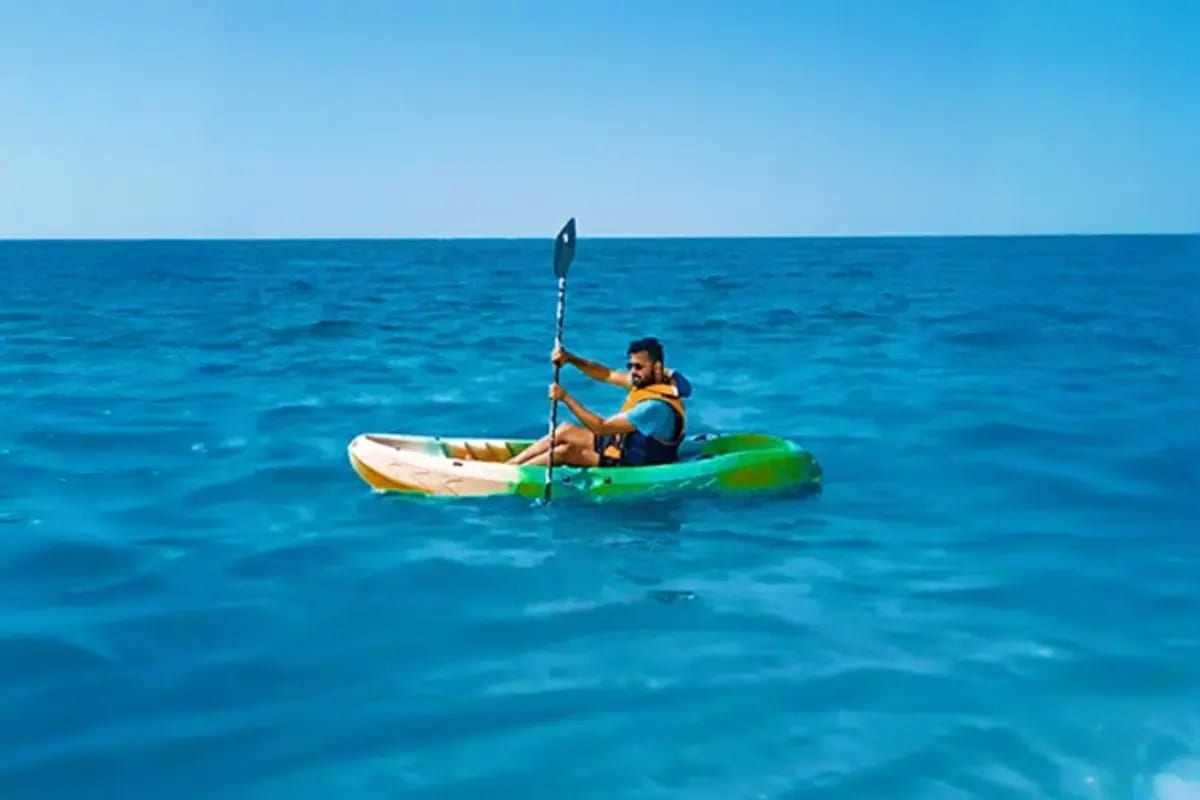 Man kayaking in turquoise ocean waters wearing yellow life jacket during water sports activity
