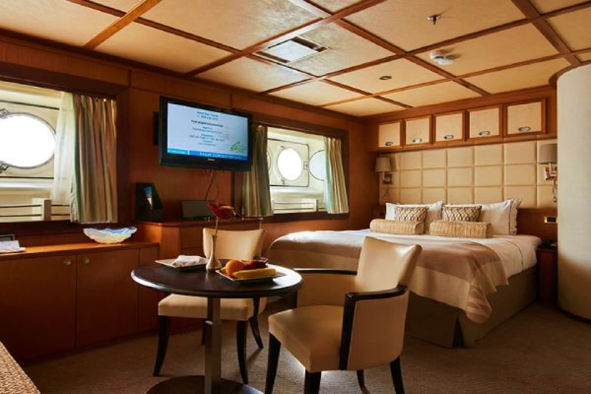 Wind Star Greek Isles Treasures Luxury cruise ship cabin with wooden paneling, queen bed, flat-screen TV, round porthole windows, and seating area with dinin