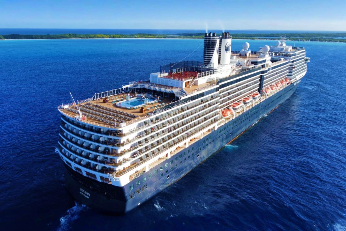 Large white cruise ship Eurodam anchored in blue ocean waters near tropical island coastline with beach and green vegetation 