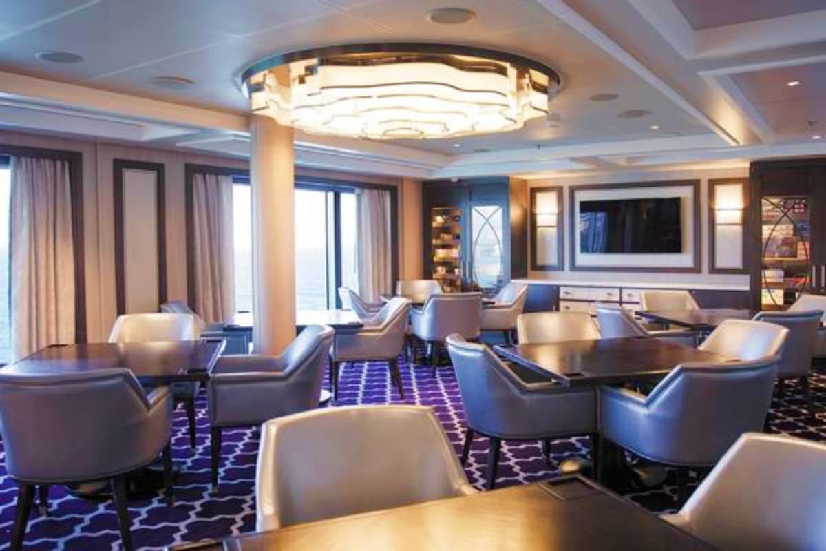 Luxury cruise ship lounge with gray seating, geometric patterned carpet, modern ceiling lights, and ocean view windows