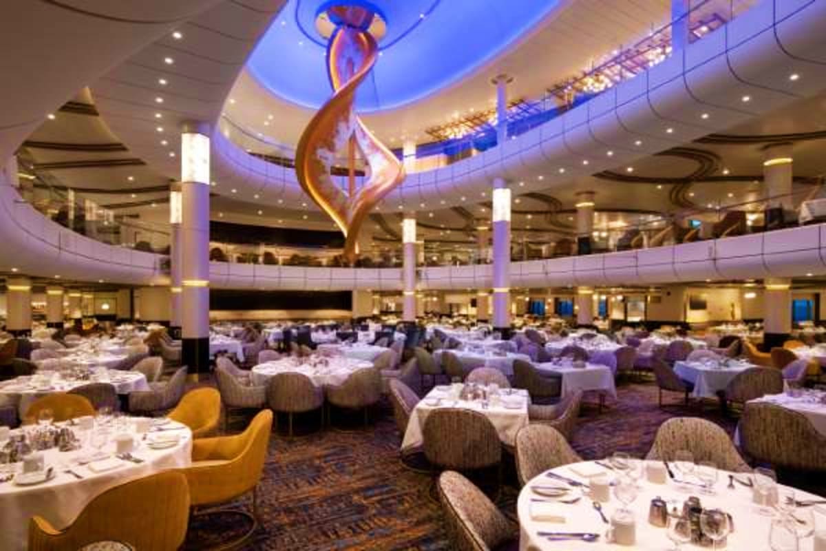 Modern multi-level dining room with white tablecloths, curved balconies, and a large illuminated bronze flame sculpture hangi