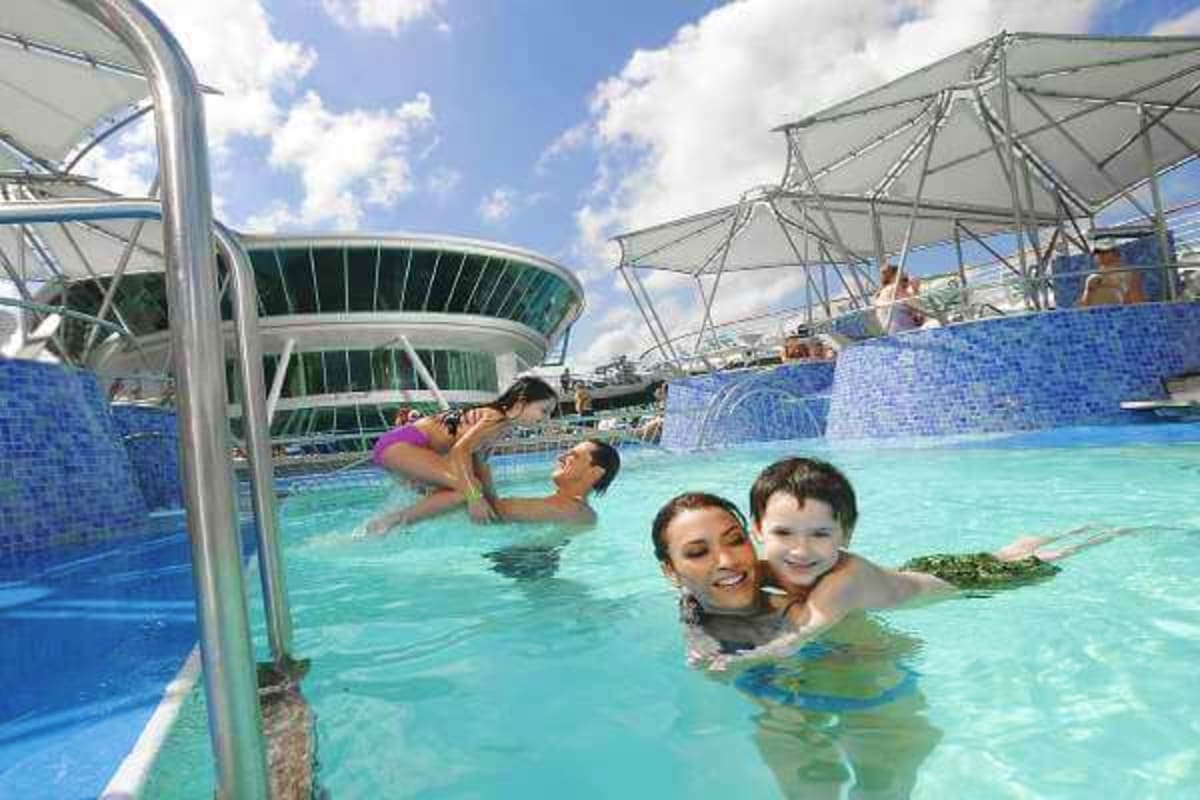 Family enjoying turquoise pool with child on shoulders at modern cruise ship waterpark with tensile sail canopies