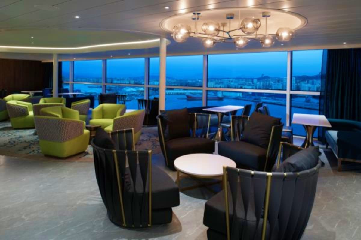 Modern lounge with floor-to-ceiling windows overlooking city lights at dusk, featuring lime green armchairs and black curved 