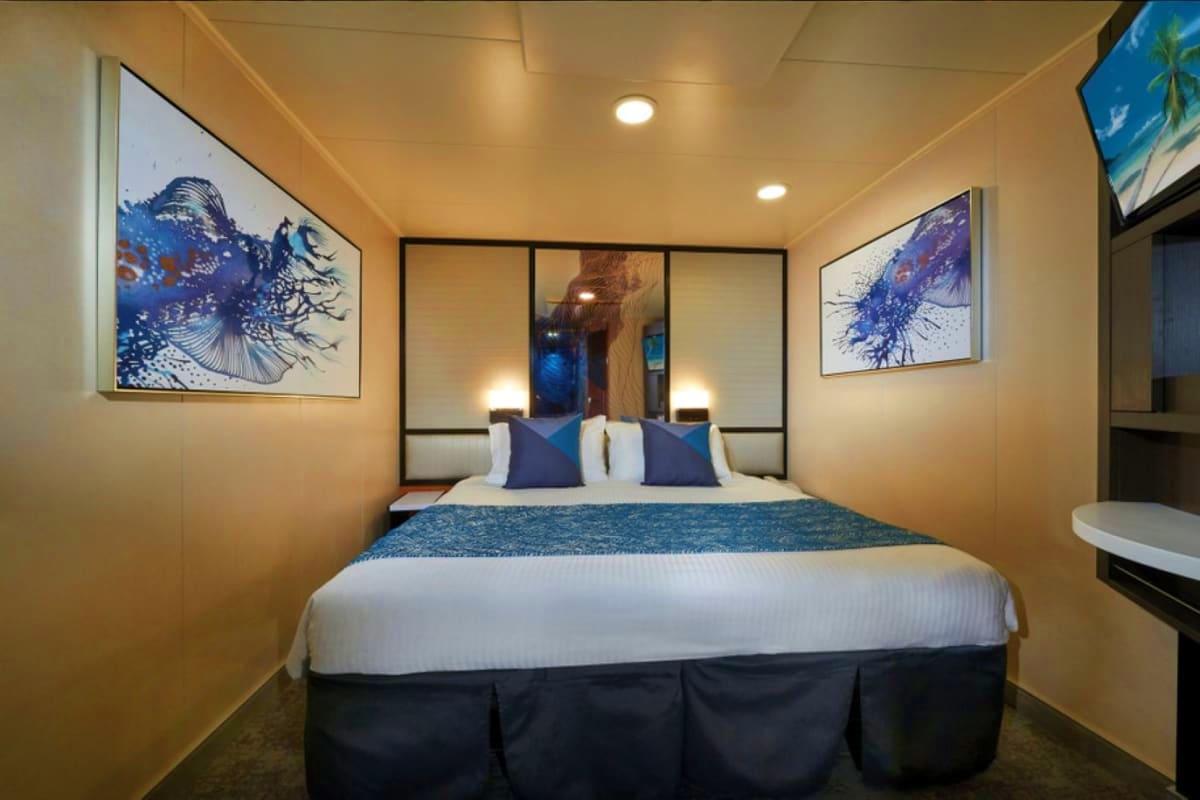 Norwegian Jade Asia Discovery Modern cruise ship cabin with queen bed, mirrored headboard, blue and white bedding, and framed abstract ocean artwork on wal