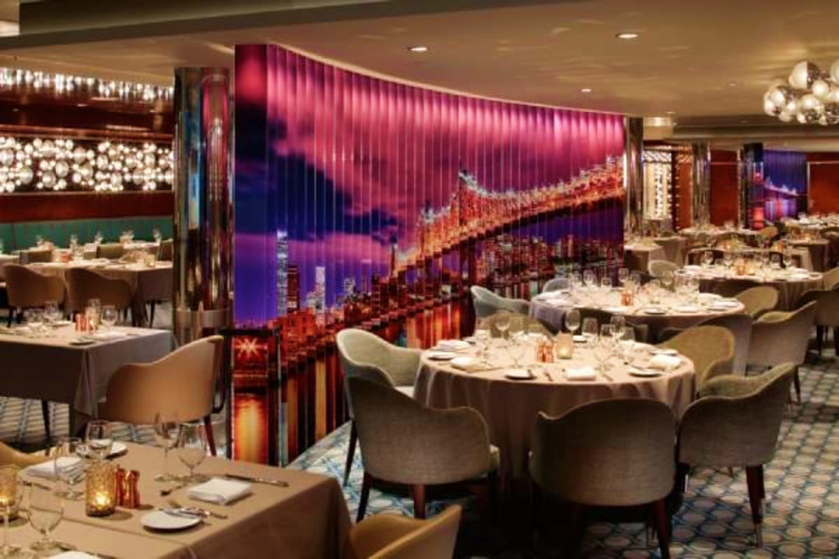 Upscale restaurant dining room with illuminated Golden Gate Bridge cityscape wall mural, round tables set with white linens, 