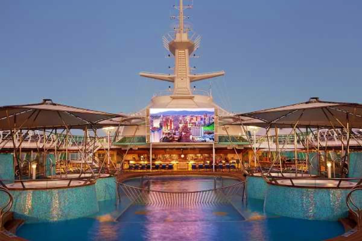 Cruise ship lido deck at dusk with swimming pools, umbrellas, and elevated bridge structure against clear sky