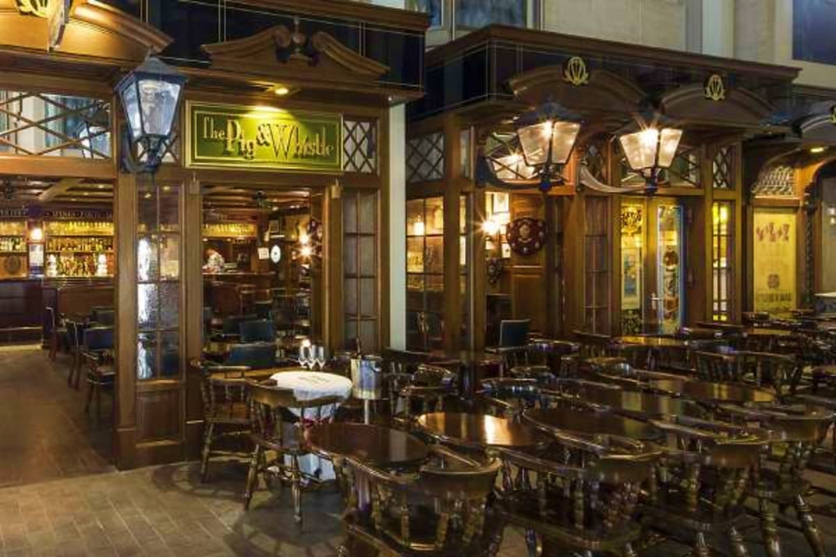 Historic pub storefront with wooden facade, brass fixtures, and outdoor seating area lit by vintage street lamps at night