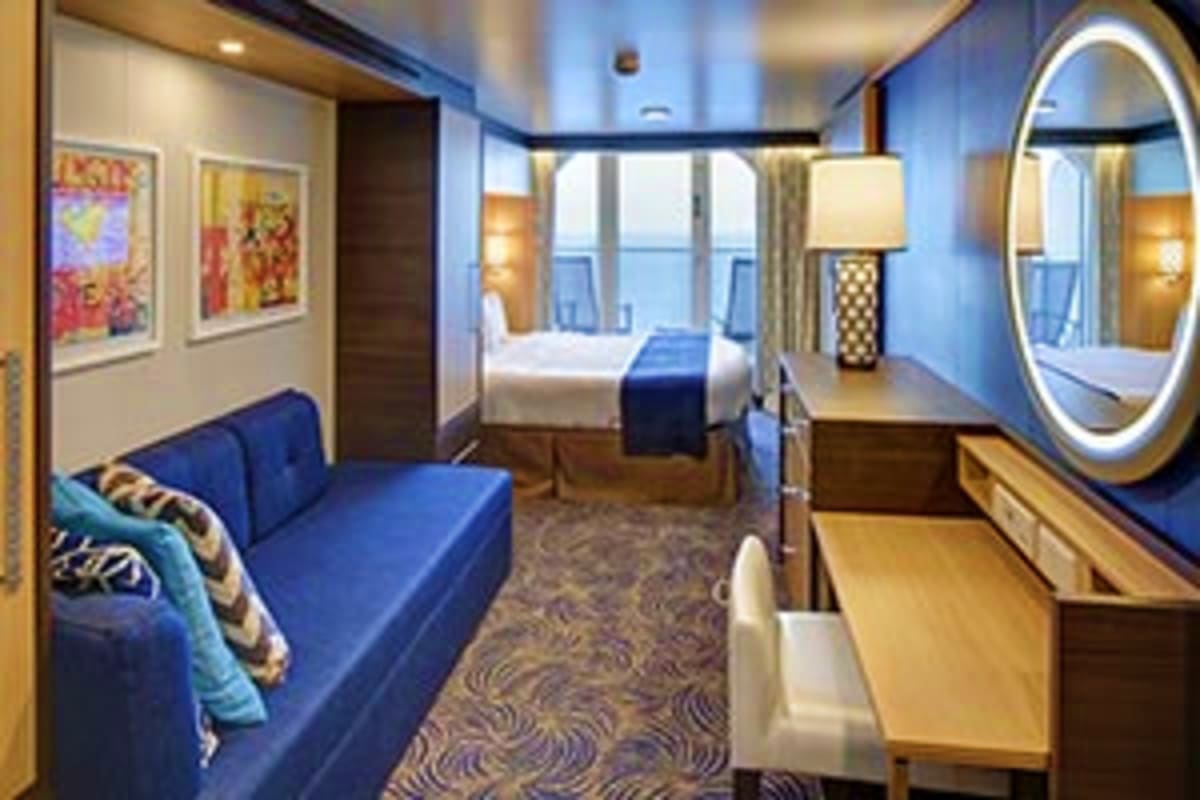 Luxurious cruise ship cabin with blue sofa, queen bed, illuminated round mirror, and ocean view windows