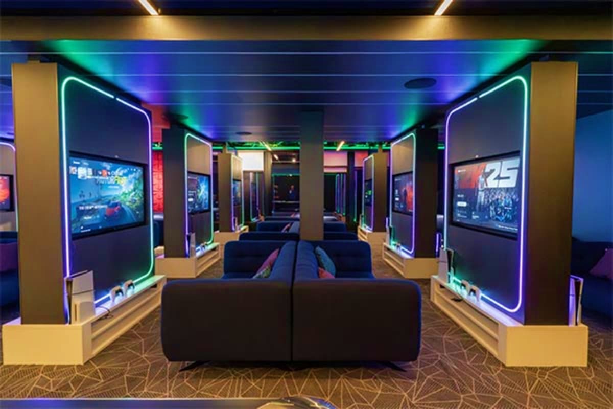 Modern gaming arcade with neon-lit gaming stations, black seating, and colorful ceiling lighting on a cruise ship interior