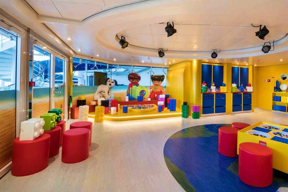 Colorful indoor play area for children with red seating pods, blue and yellow storage units, LEGO figures, and floor-to-ceili