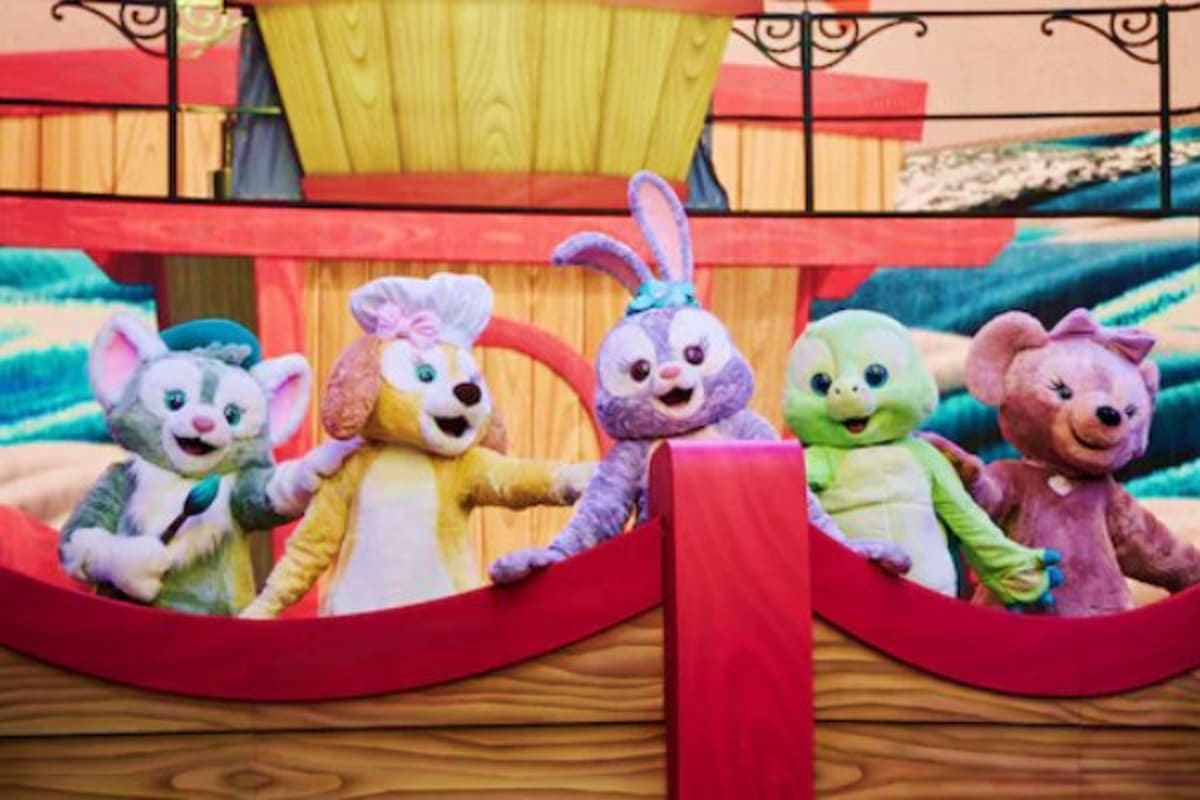 Five colorful plush character mascots performing on a red stage with Asian-inspired architecture and wooden details in backgr