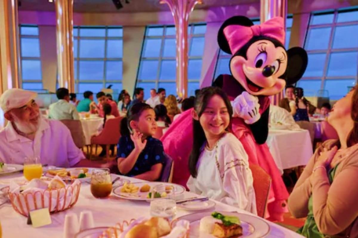 Minnie Mouse character dining with families at a cruise ship restaurant with ocean views and purple ambient lighting