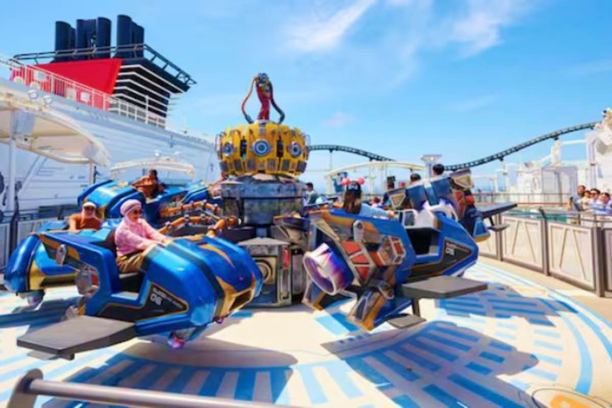 Passengers enjoying blue and gold ride vehicles on a cruise ship deck with a yellow crowned attraction structure and Disney c