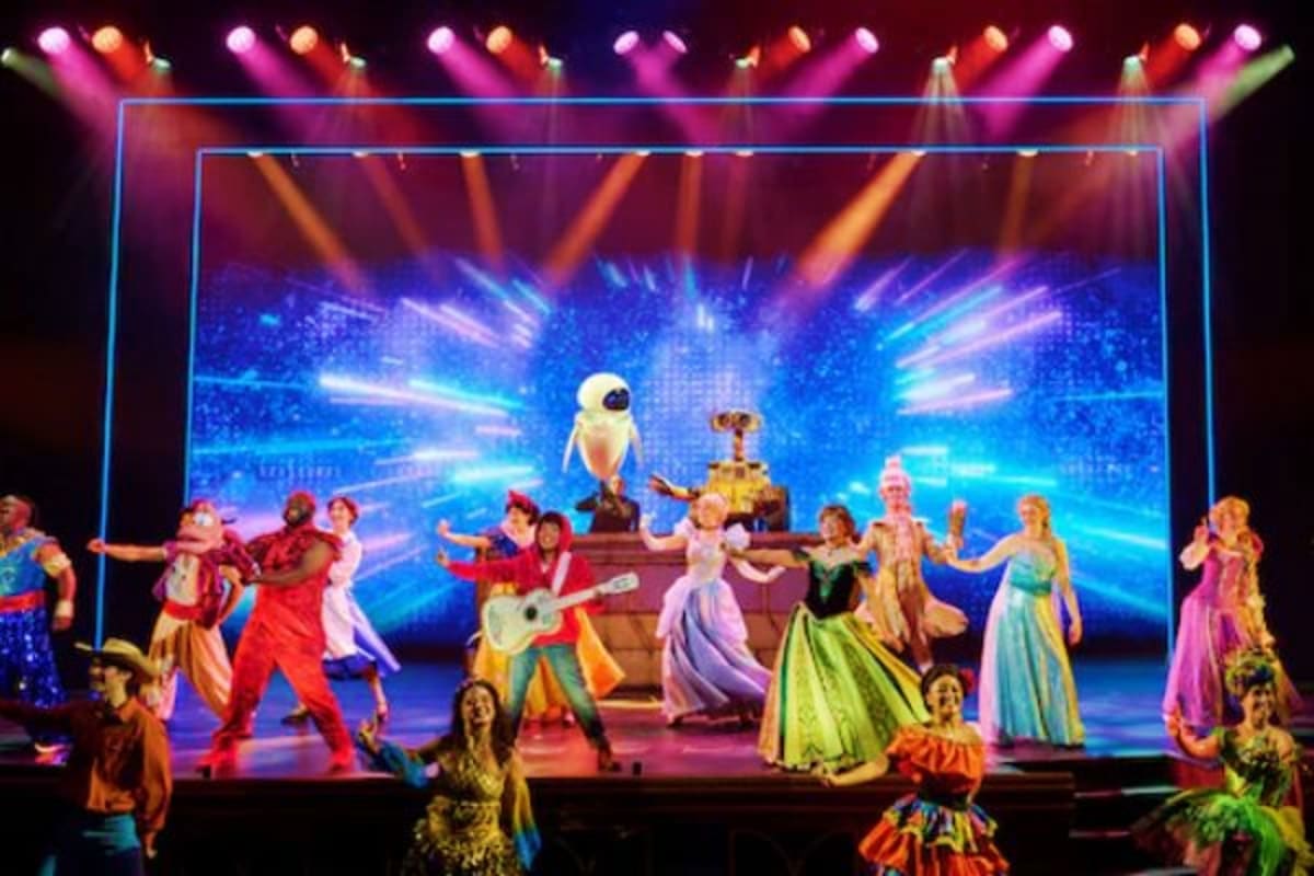 Stage performance of Disney characters and animated robots dancing under colorful stage lights with neon blue backdrop on cru