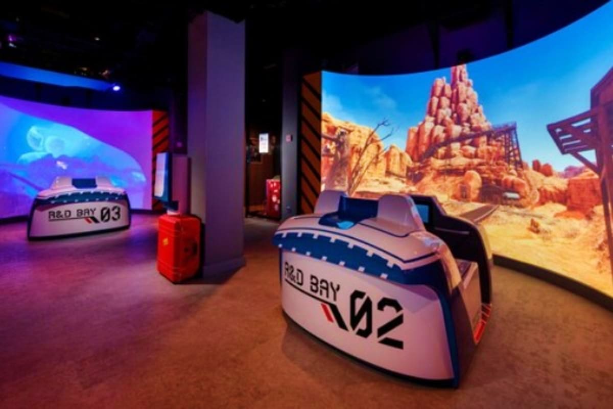 Interactive racing car simulator attraction with desert landscape display in themed entertainment venue