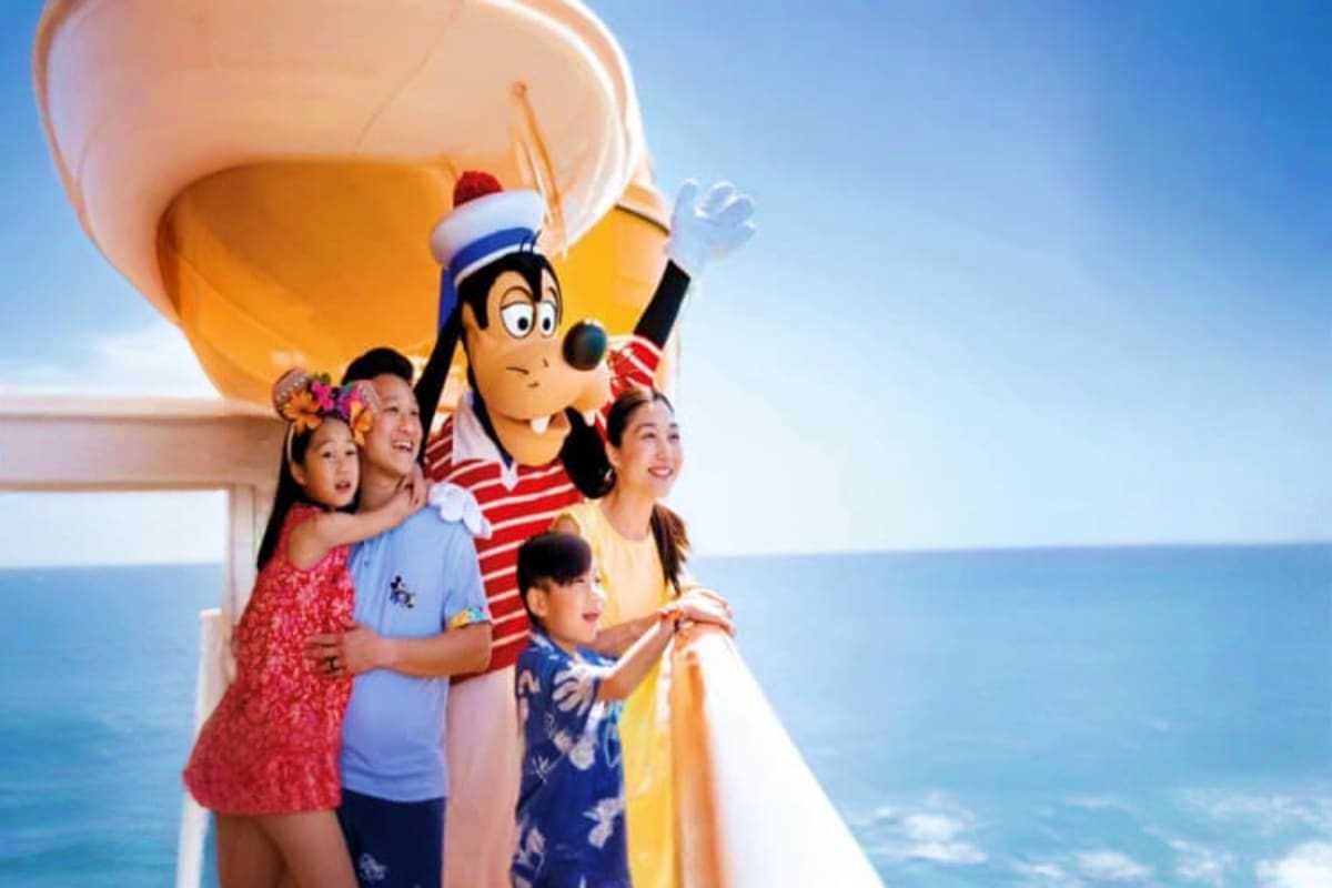 Family with cartoon sailor character on Disney cruise ship deck with ocean and white sails in background