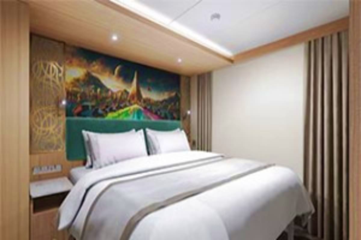 Four Nights Disney Island Escape Modern cruise ship cabin bedroom with white bedding, green headboard, mountain landscape artwork, and neutral wood and beige