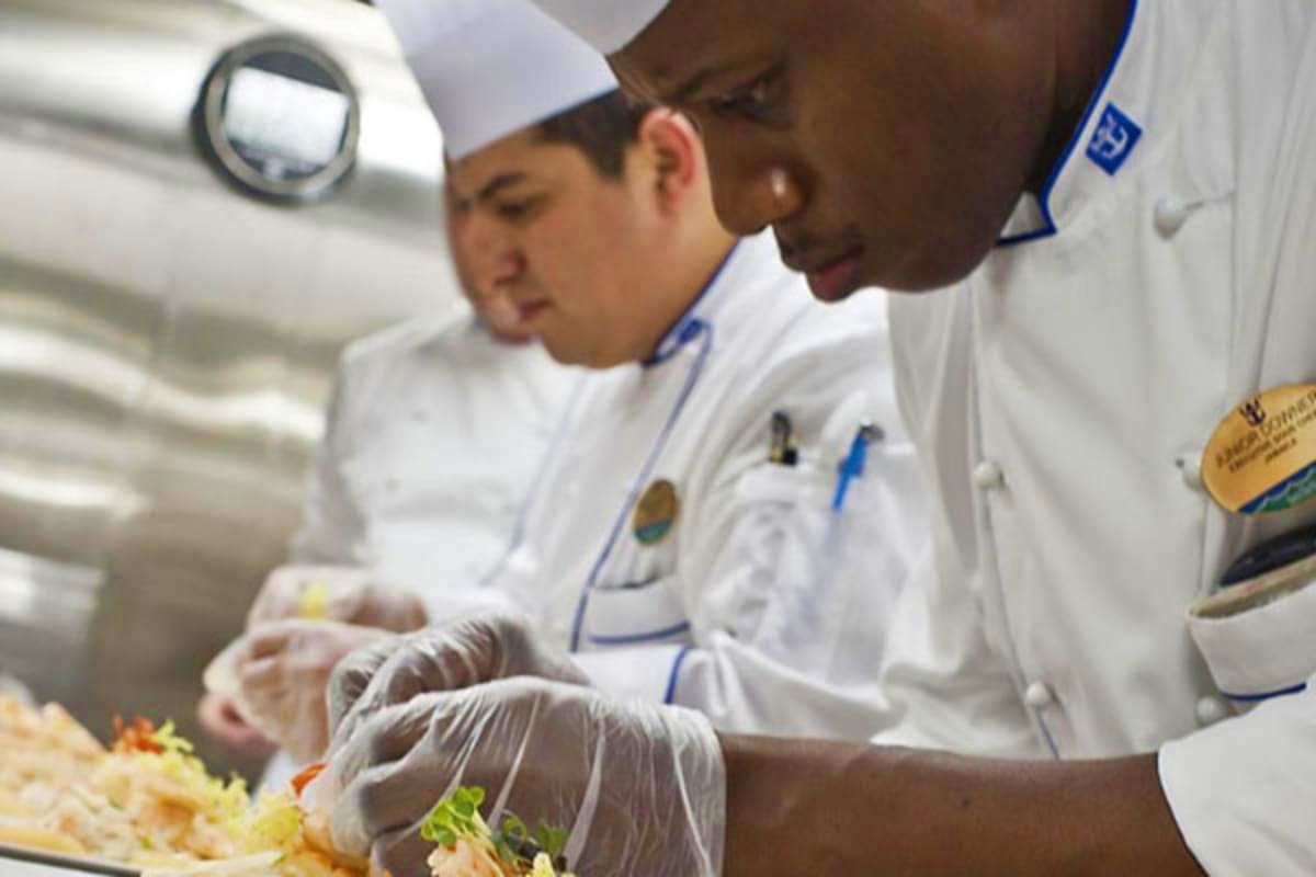 Southeast Asia Cruise Escape Professional chefs in white uniforms and gloves preparing and plating gourmet dishes in a ship's kitchen galley