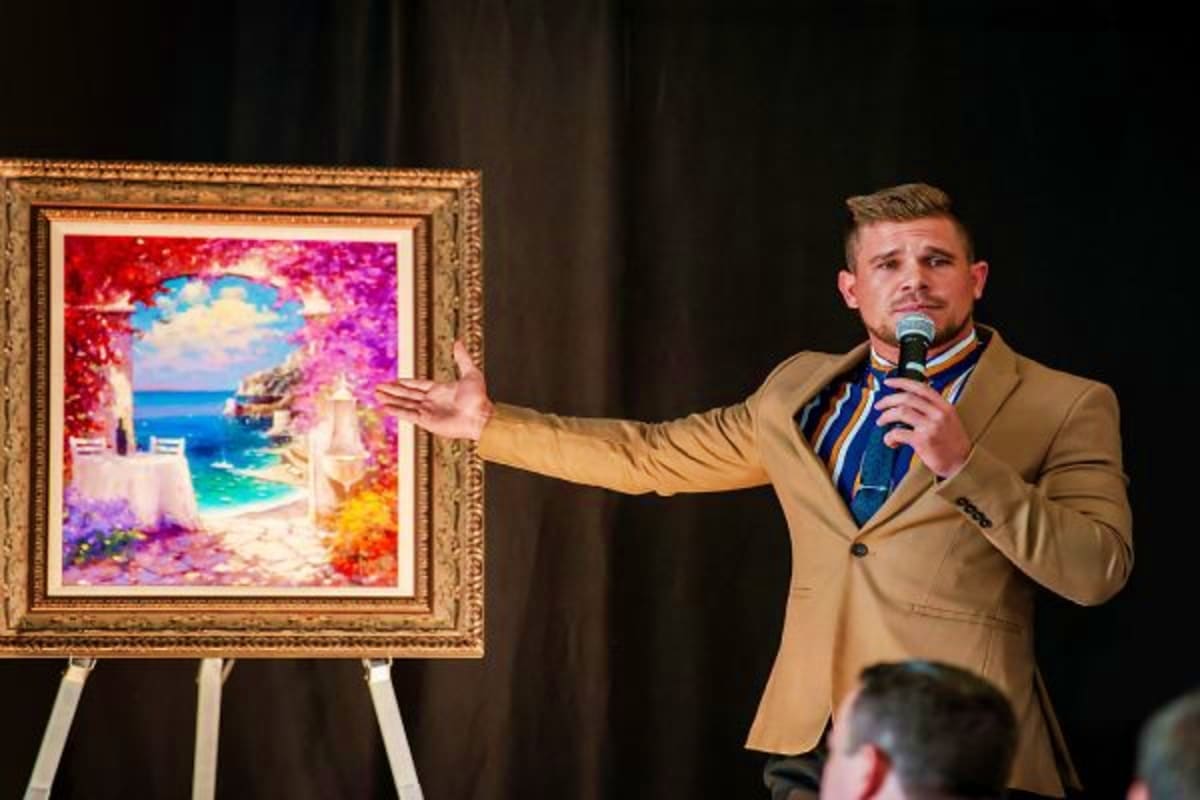 Southeast Asia Cruise Escape Man in beige blazer presenting framed colorful artwork of Mediterranean coastal villa with turquoise sea and vibrant flowers