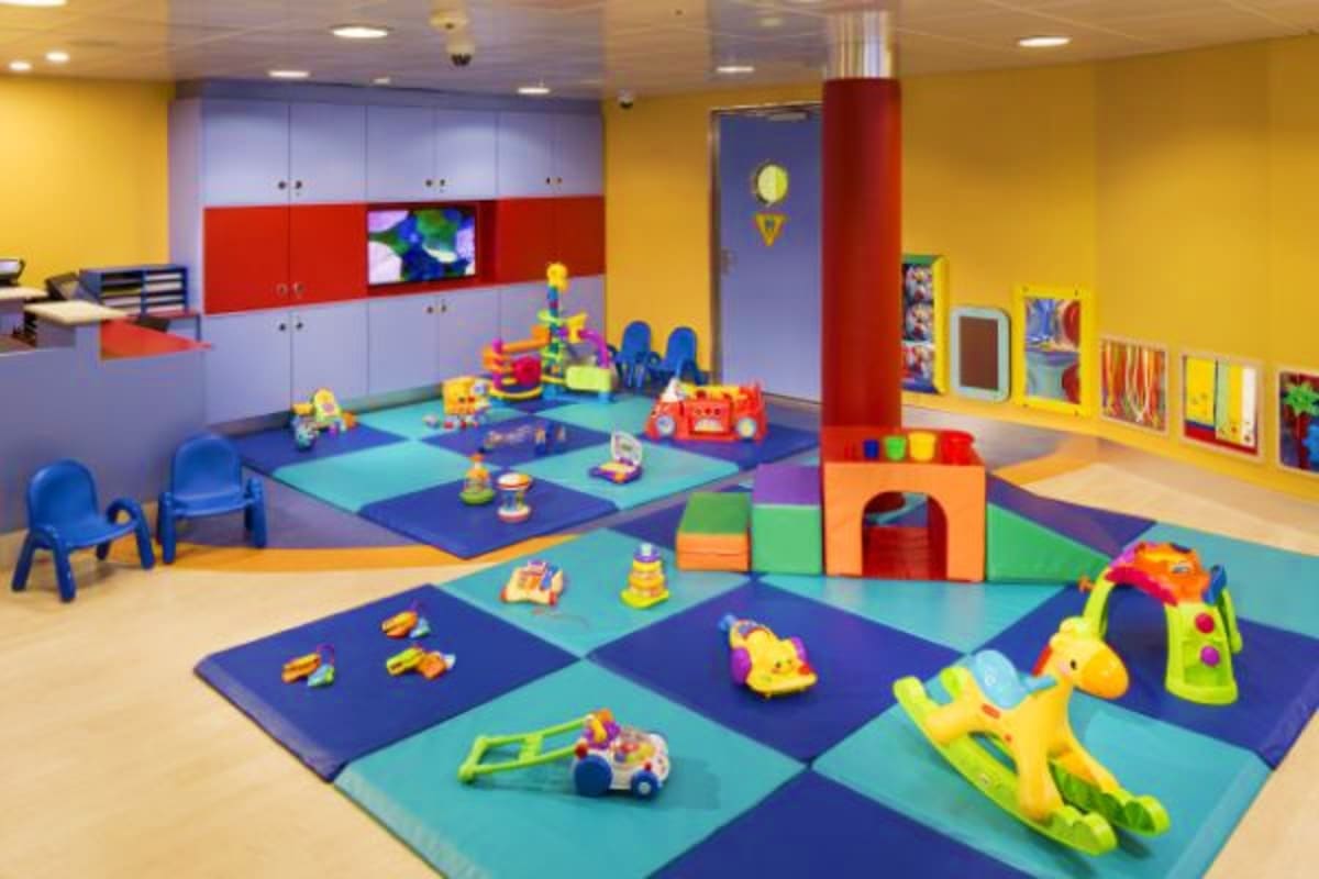 Bright, colorful indoor daycare or nursery room with foam play mats, toys, storage cabinets, and educational materials on yel