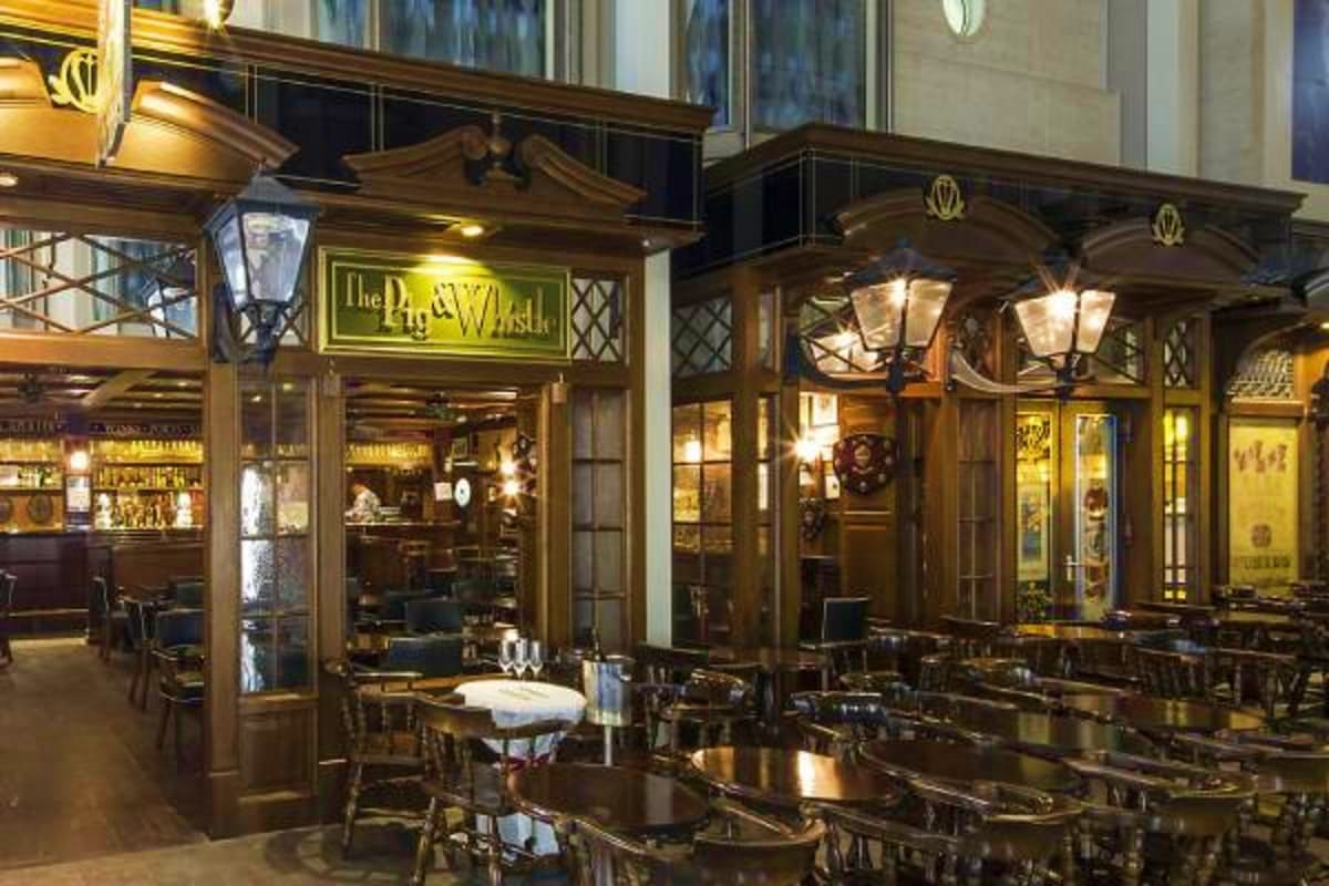 Elegant wooden storefront with "The Plaza Walk" sign and outdoor dining area with black tables and chairs, lit by vintage-sty