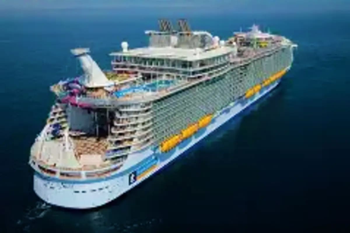 Singapore to Samurai Shores Large cruise ship at sea with white hull, blue and yellow stripe, viewed from aerial angle on calm ocean water