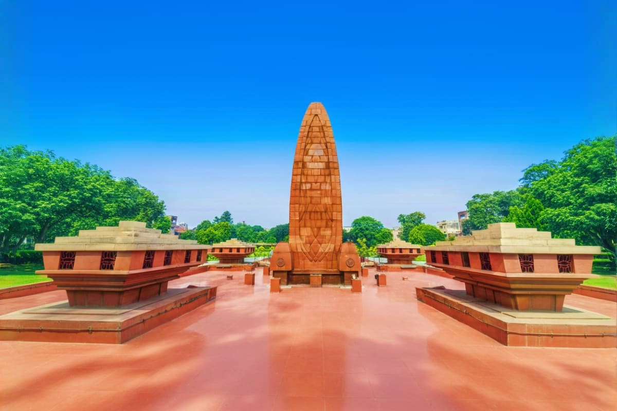Jallianwala Bagh memorial monument with red brick buildings and manicured gardens under clear blue sky in Amritsar, India