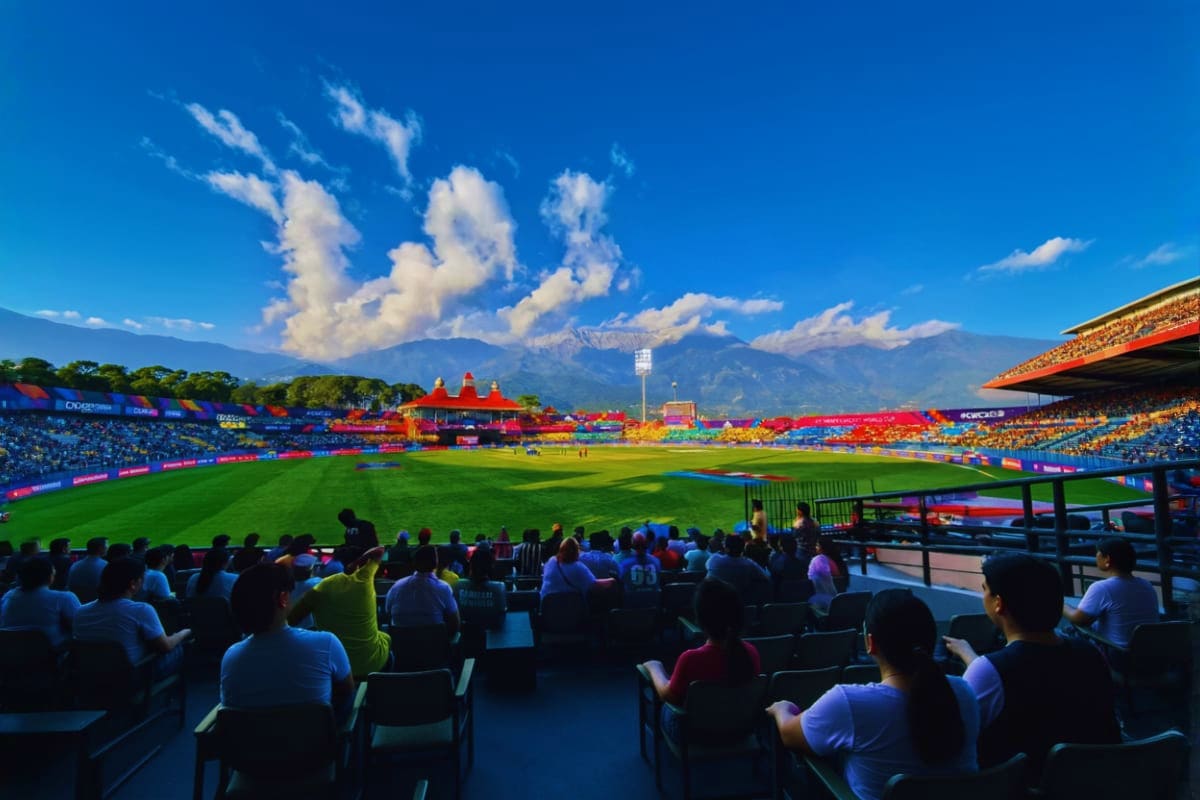 Crowded stadium with colorful banners, green football field, and snow-capped Himalayan mountains in background under blue sky