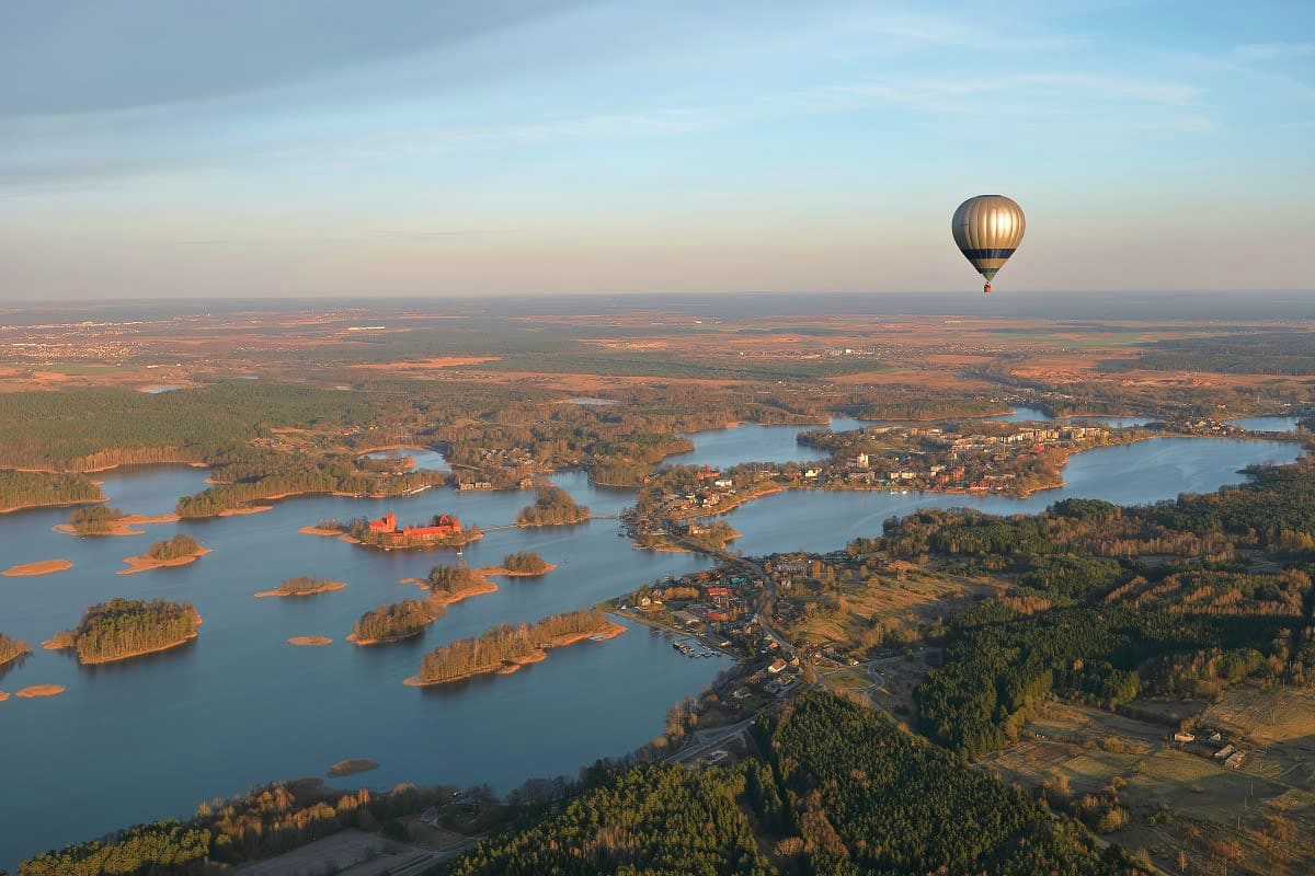 Lithuania Highlights Getaway Hot air balloon floating above scenic Finnish lake landscape with forested islands and scattered houses below at sunrise