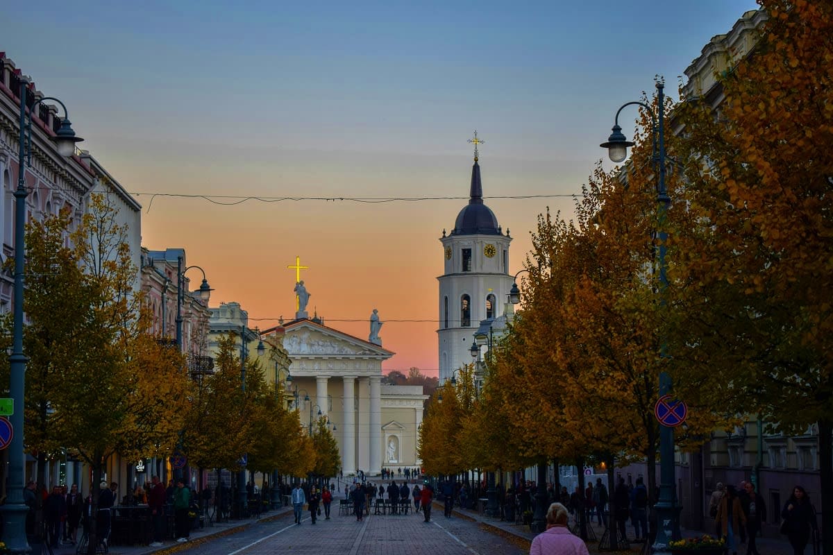 Lithuania Highlights Getaway Cathedral Square in Vilnius during autumn with white church building and bell tower at sunset, crowds of pedestrians walking
