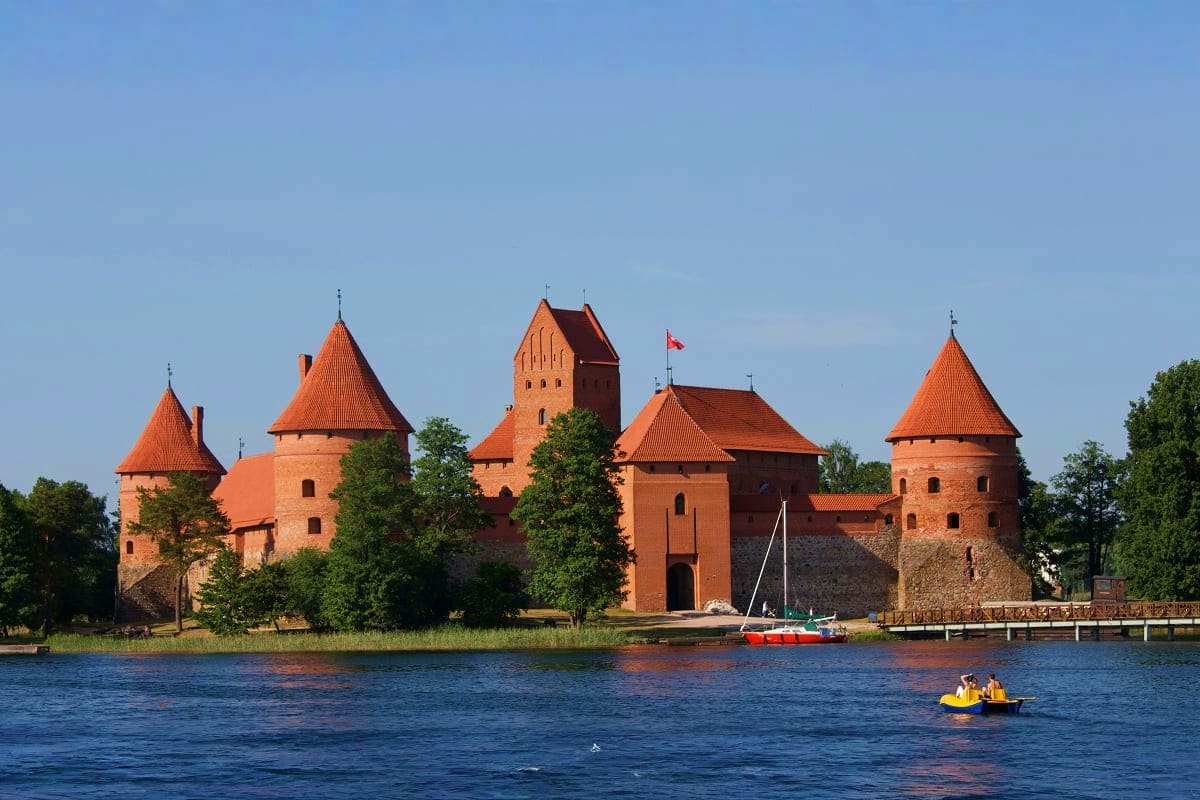 Lithuania Highlights Getaway Trakai Castle medieval fortress with red brick towers and orange roofs on a lake in Lithuania with sailboat and tourists