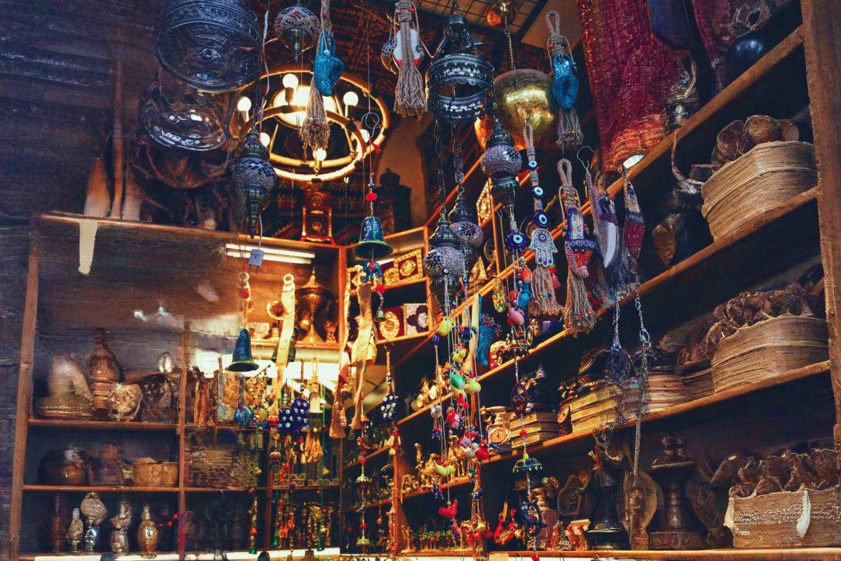 Ornate Middle Eastern souk shop display with hanging brass lanterns, decorative metal vessels, tasseled ornaments, and tradit