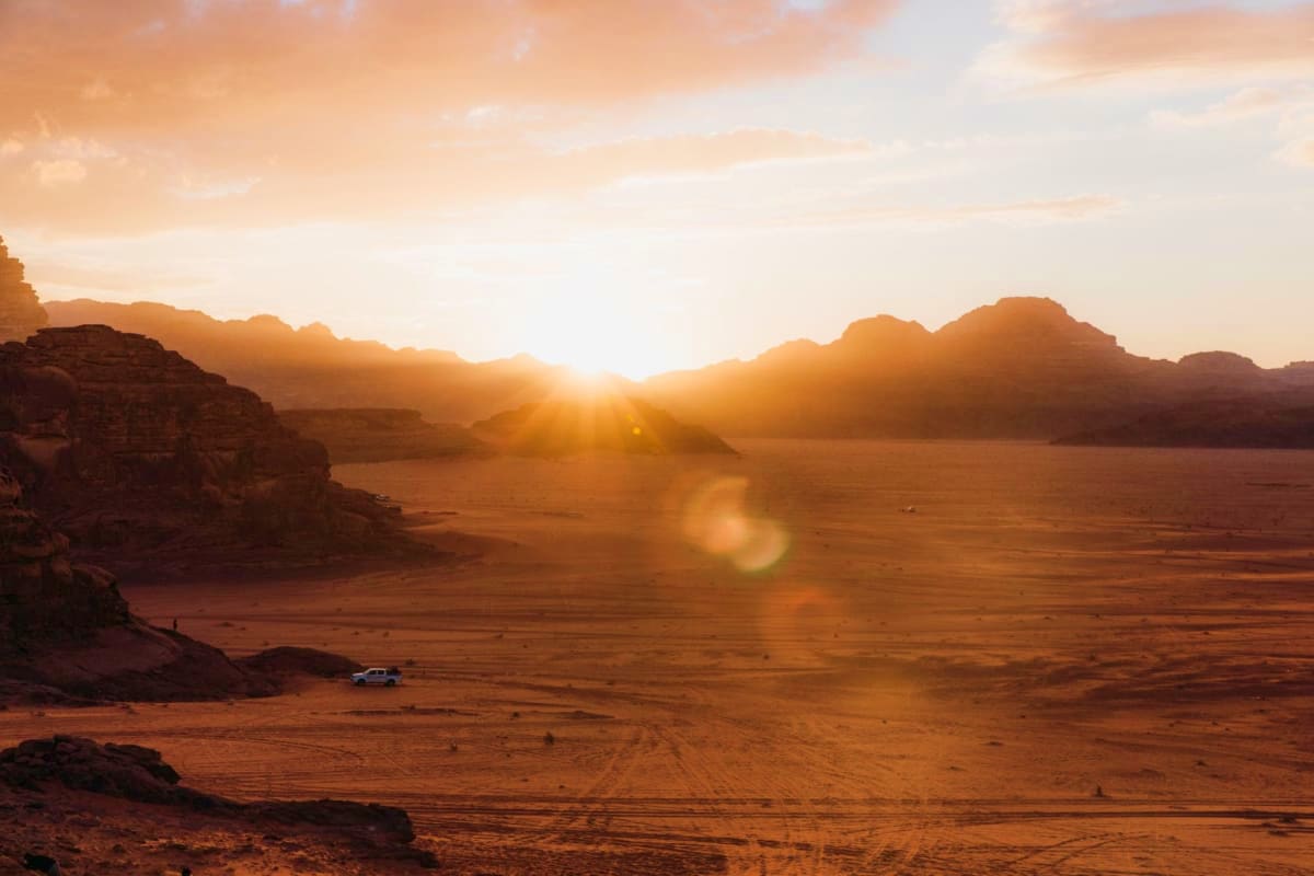 Sunrise over Wadi Rum desert landscape with golden light illuminating red rock formations and a vehicle on sandy terrain