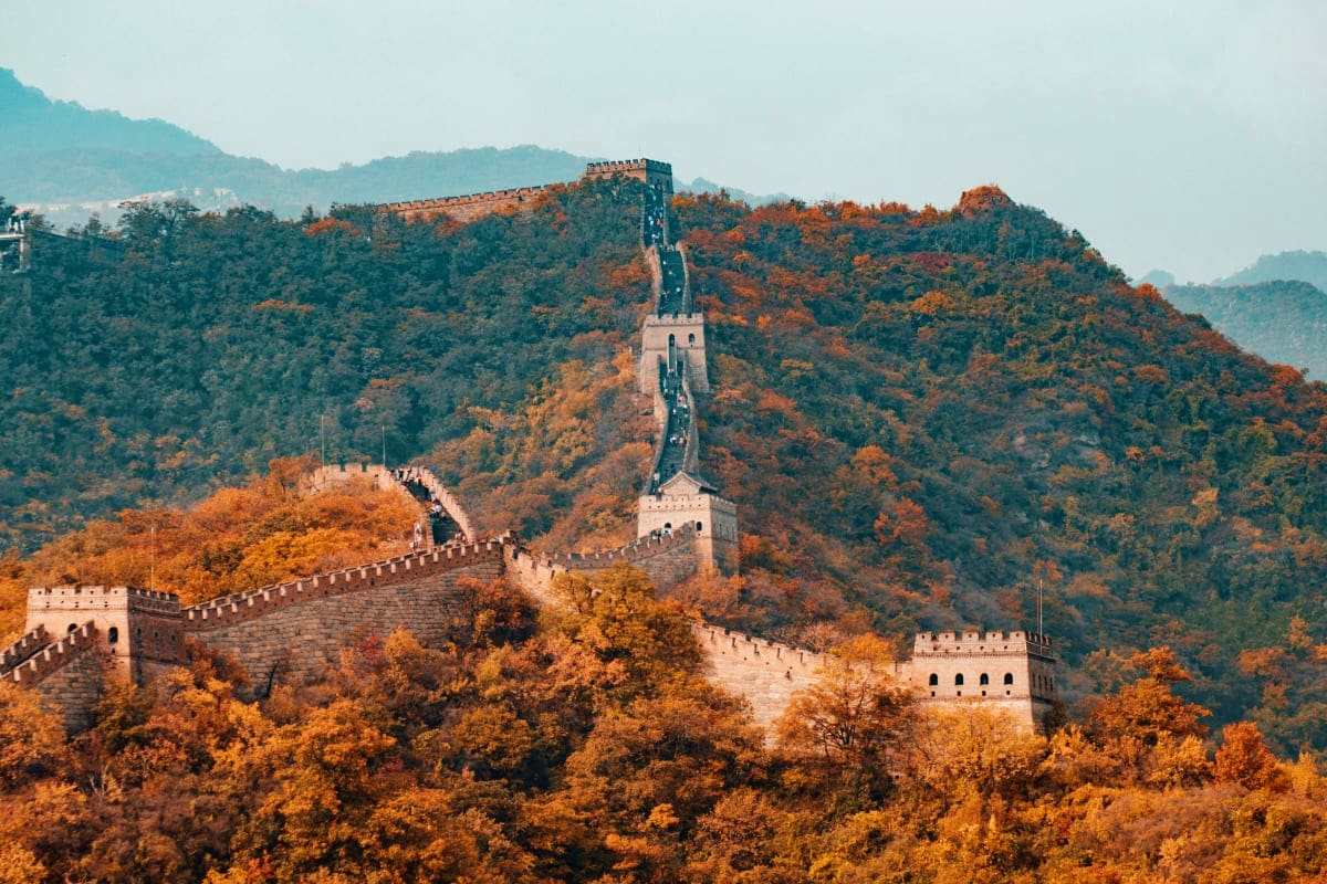 Great Wall of China stretching across forested mountains in autumn with golden foliage and watchtowers visible along the ridg
