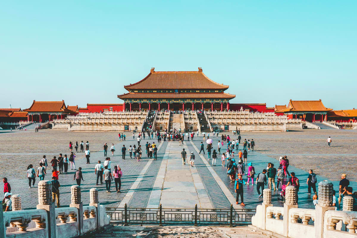 Tourists walking across the courtyard of the Forbidden City in Beijing with traditional Chinese architecture and golden roofs