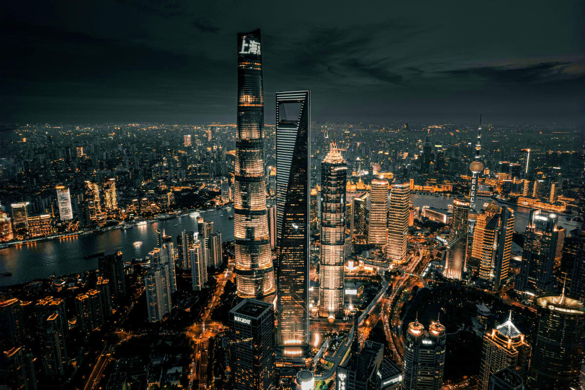 Aerial nighttime view of Shanghai skyline with illuminated skyscrapers, Huangpu River, and cityscape at dusk