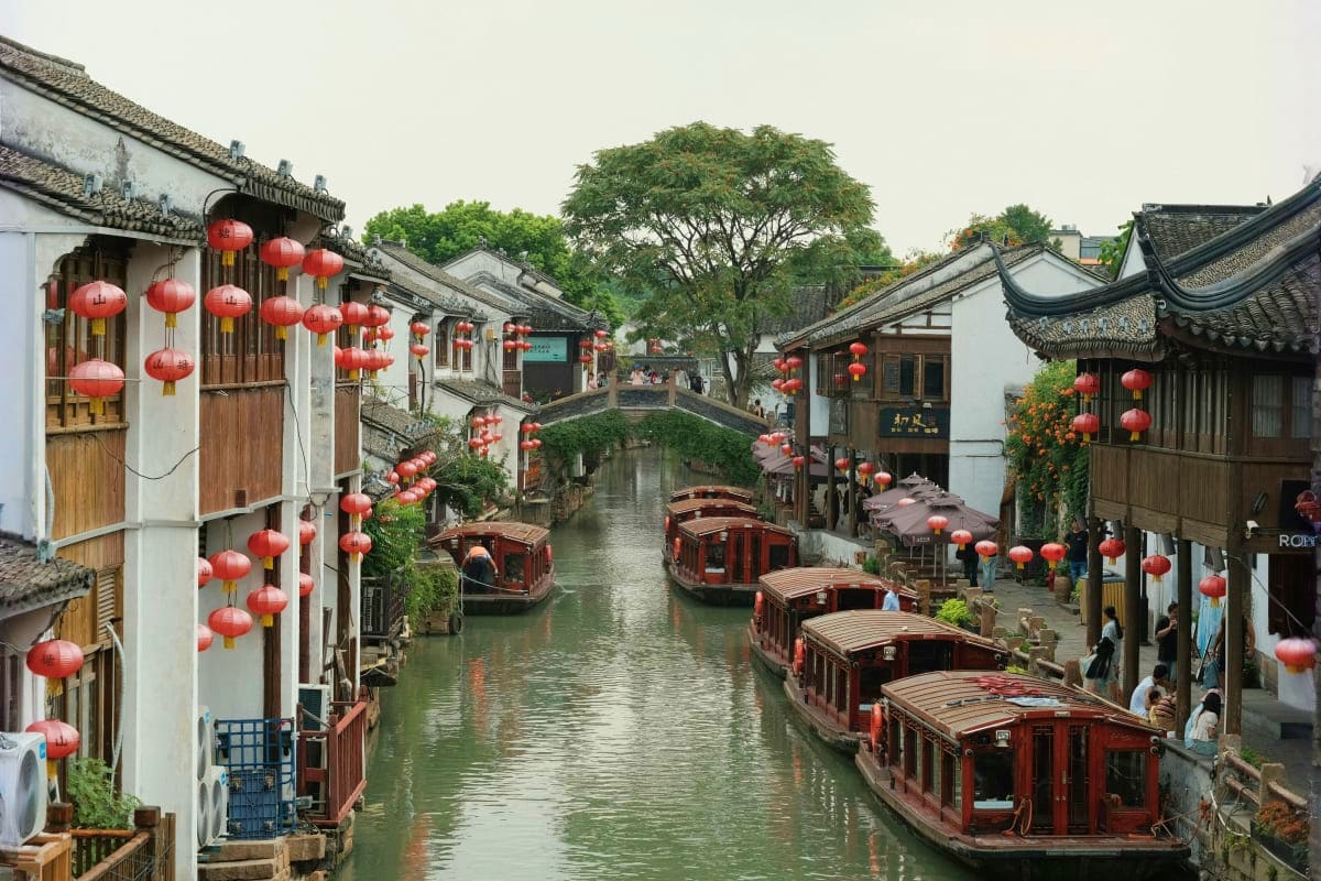Traditional Chinese watertown with red lanterns, wooden boats, and historic architecture along a canal