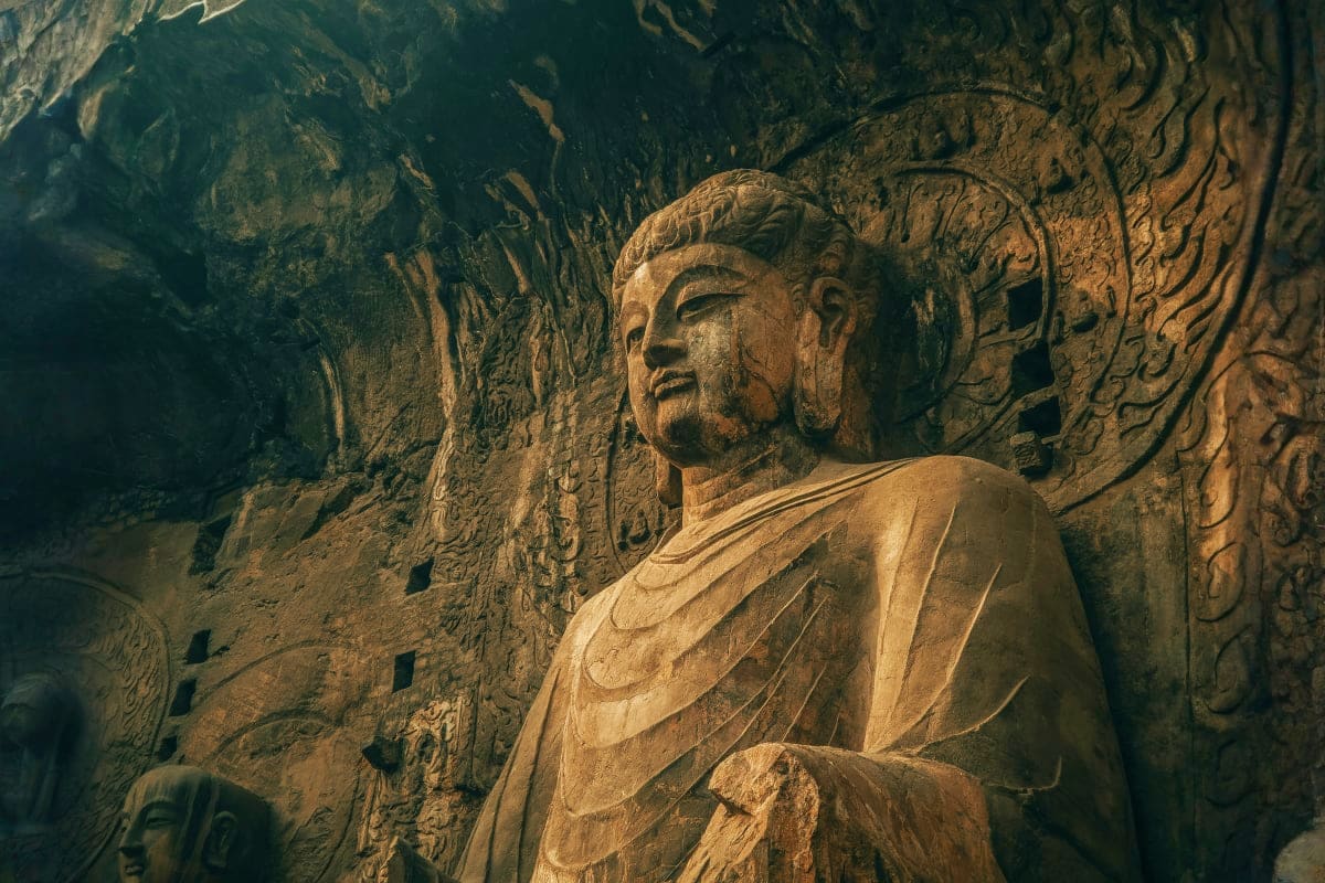 Ancient Buddhist stone carving of robed figure in cave temple with intricate relief sculptures on surrounding walls at Longme