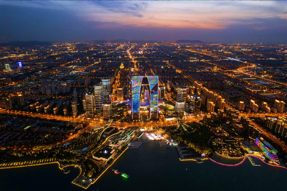 Aerial night view of illuminated Chengdu cityscape with glowing skyscrapers, river, and city lights at dusk