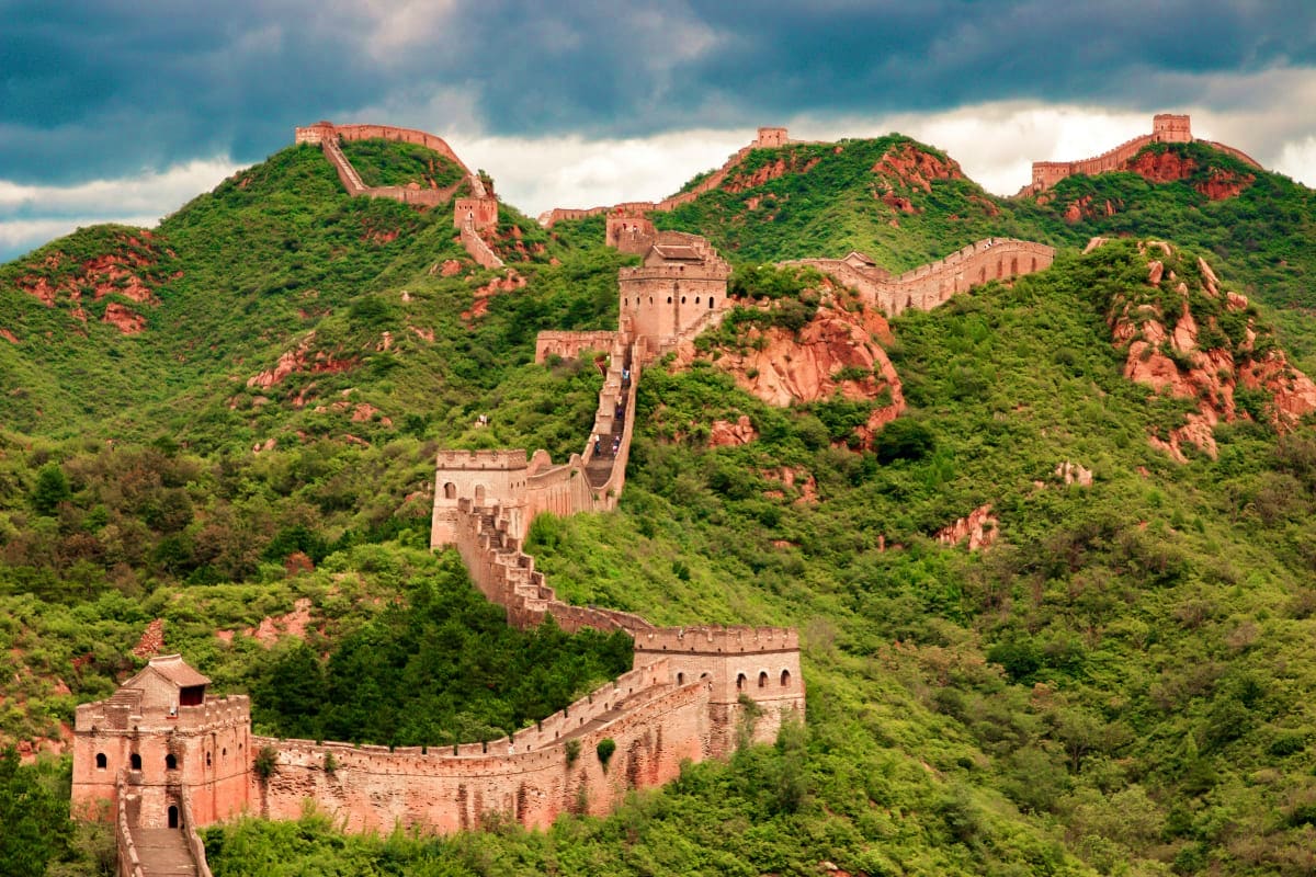 Great Wall of China winding through forested mountains with restored brick watchtowers and fortifications under cloudy sky