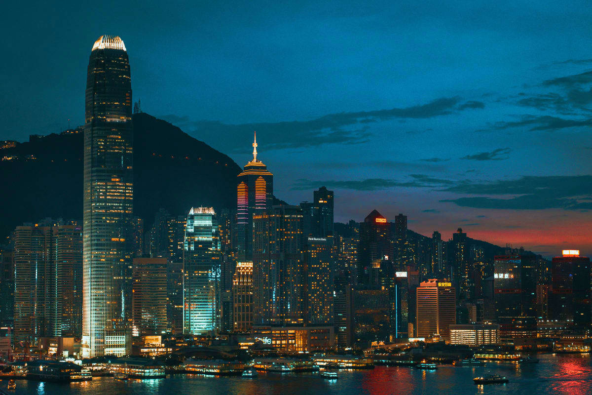 Hong Kong skyline at twilight with illuminated skyscrapers, Victoria Harbor, and mountains in the background at dusk