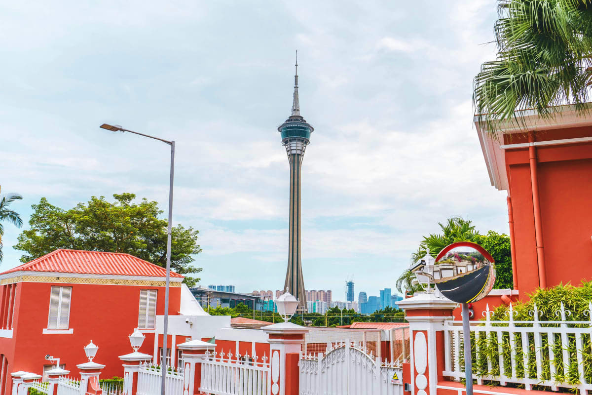 Kuala Lumpur Tower visible beyond red and white colonial-style buildings with palm trees in foreground