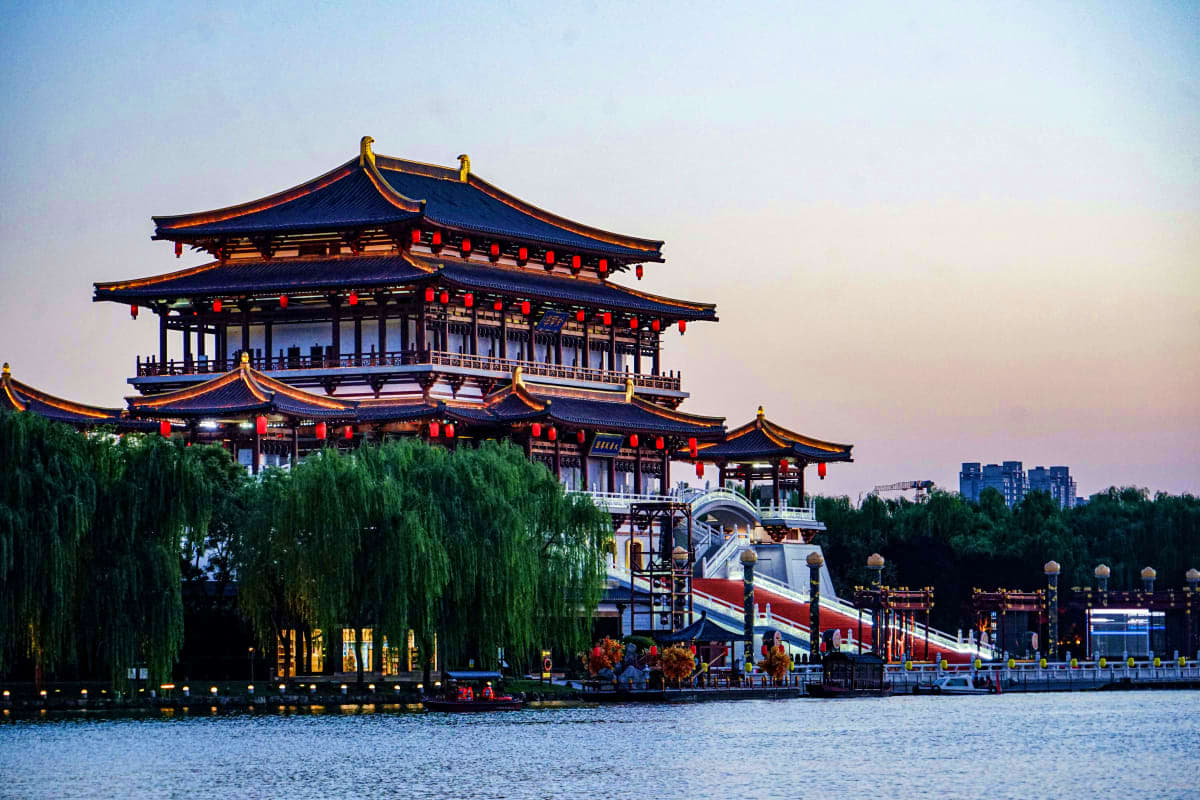 Traditional Chinese pagoda with upturned eaves and red lanterns overlooking a waterway at dusk in Shanghai