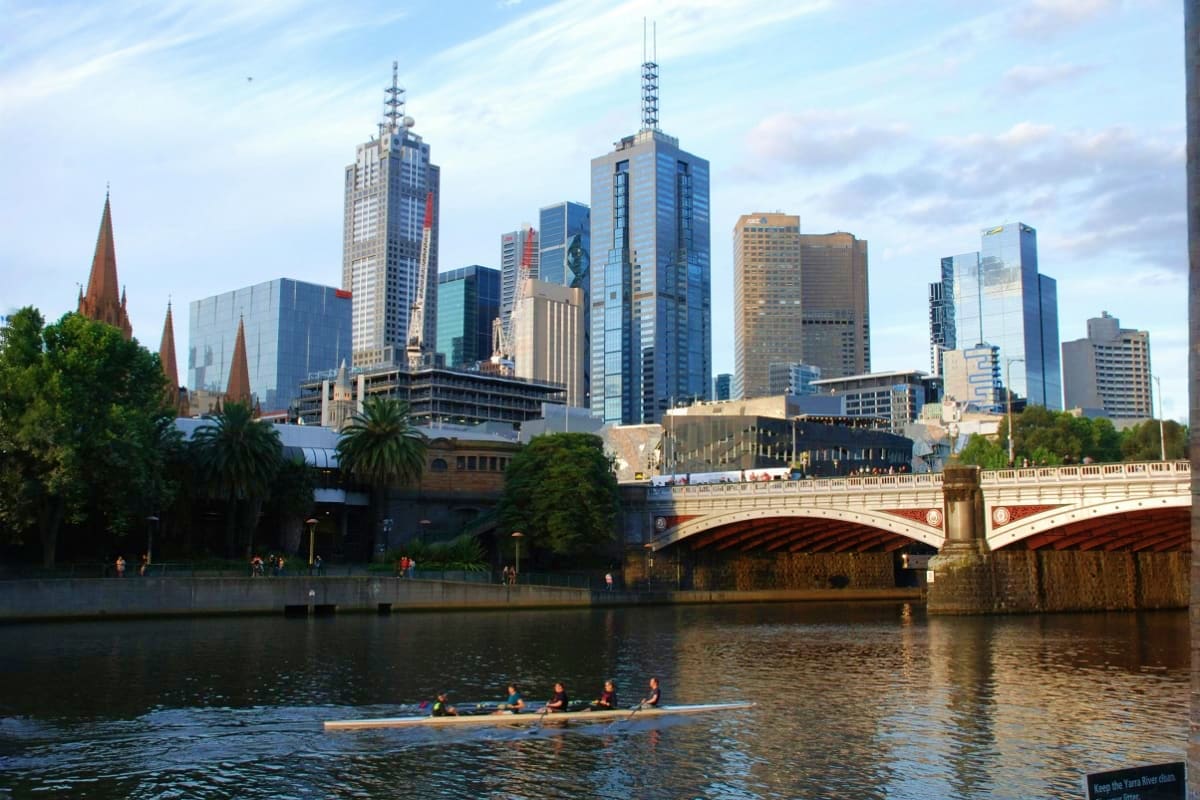 Melbourne skyline with Yarra River, historic bridge, and rowing team on water