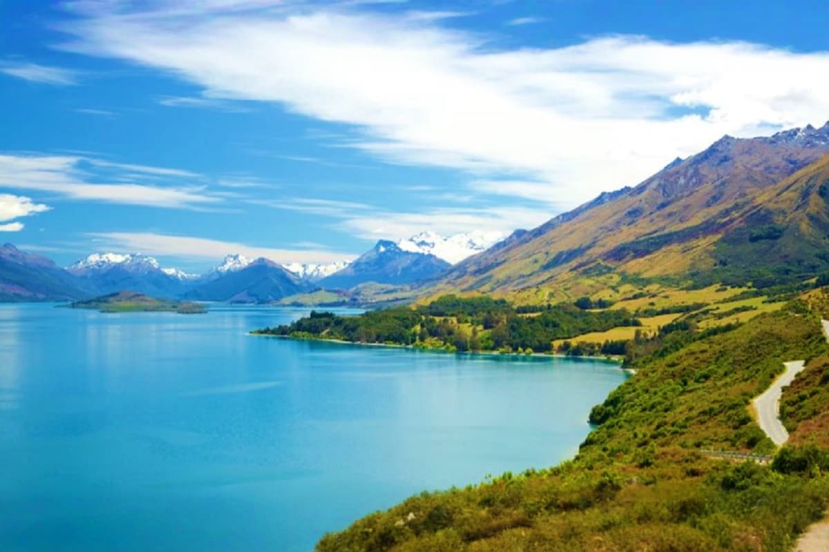 South Island Tour of New Zealand – 5 nights & 6 days Turquoise lake surrounded by snow-capped mountains, forested hillsides, and winding road in New Zealand's South Island